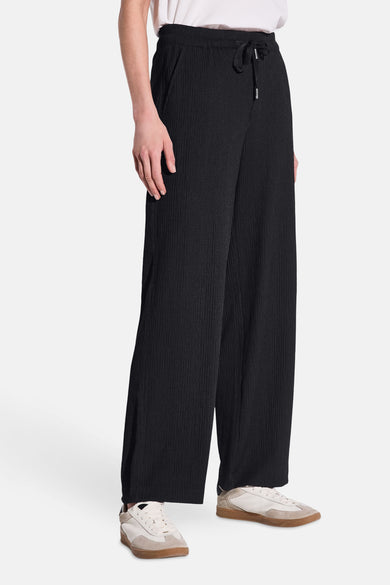 Pantalon noir à jambe large de STREET ONE, avec cordon de serrage et des baskets blanches.
