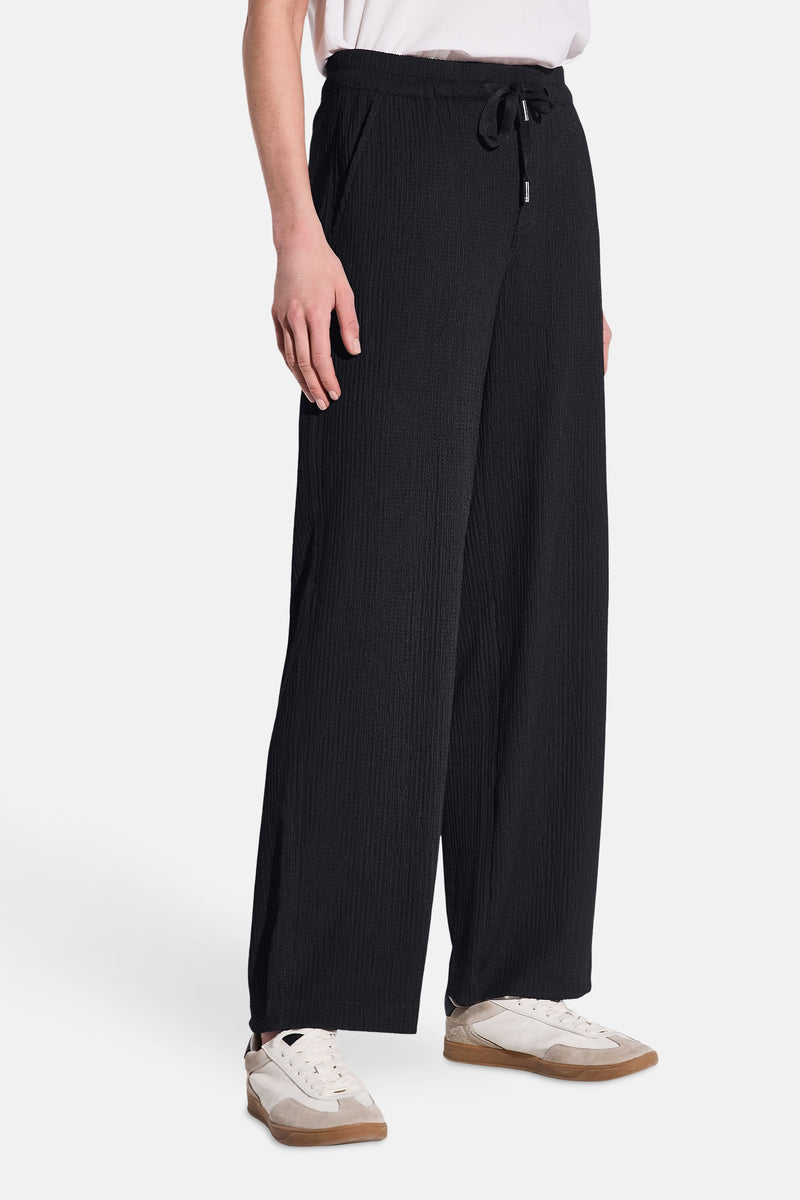 Pantalon noir à jambe large de STREET ONE, avec cordon de serrage et des baskets blanches.
