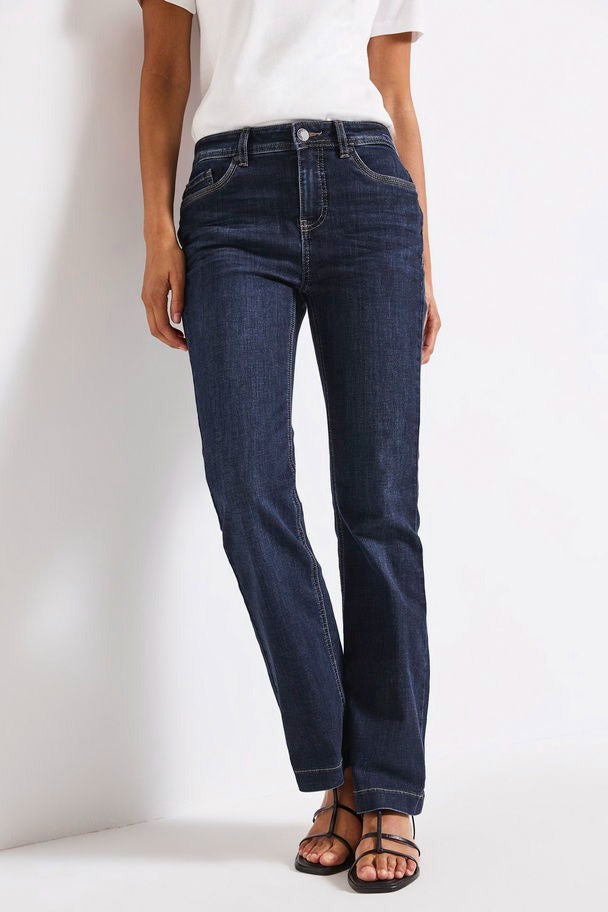 Jean bootcut en denim bleu foncé de Street One, porté avec un t-shirt blanc uni et des sandales noires.