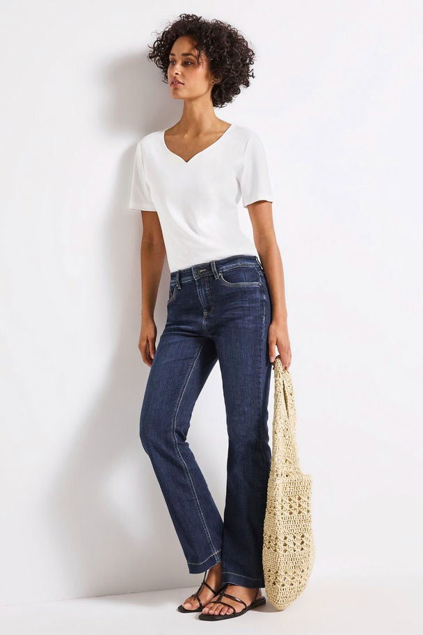 Jean bootcut en denim bleu foncé de Street One, porté avec un t-shirt blanc et des sandales noires.