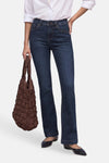 Jean bootcut en denim bleu foncé de STREET ONE, porté avec une chemise blanche, un sac matelassé marron et des chaussures plates noires.