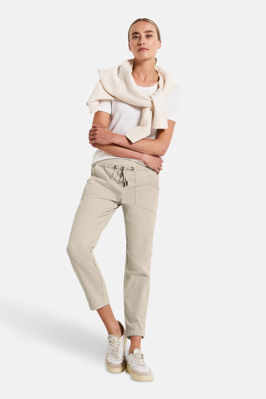 Pantalon coloré écru de Street One, porté avec un t-shirt blanc et un pull en tricot sur les épaules.
