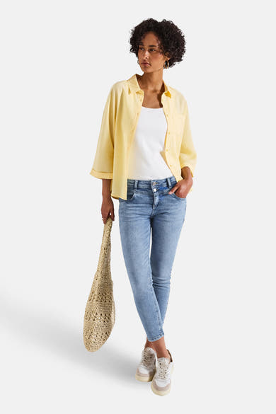 Slim jeans in lichtblauw denim van Street One, gedragen met een gele blouse en een beige tas.