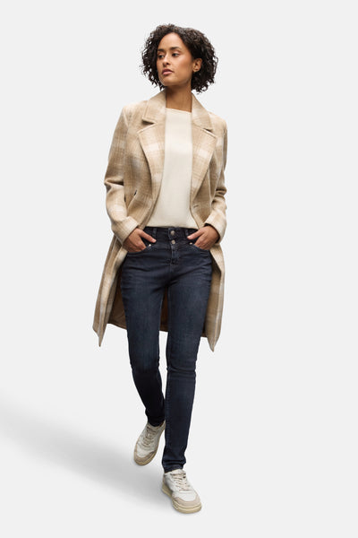 Slim jeans in zwartblauw denim van Street One, gedragen met een beige geruite jas en witte sneakers.