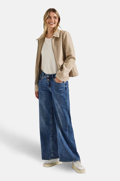 Wijde spijkerbroek in middieblauw denim van Street One, gedragen met een gebroken wit T-shirt en een beige jas.