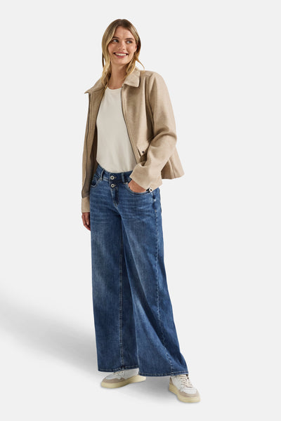 Wijde spijkerbroek in middieblauw denim van Street One, gedragen met een gebroken wit T-shirt en een beige jas.