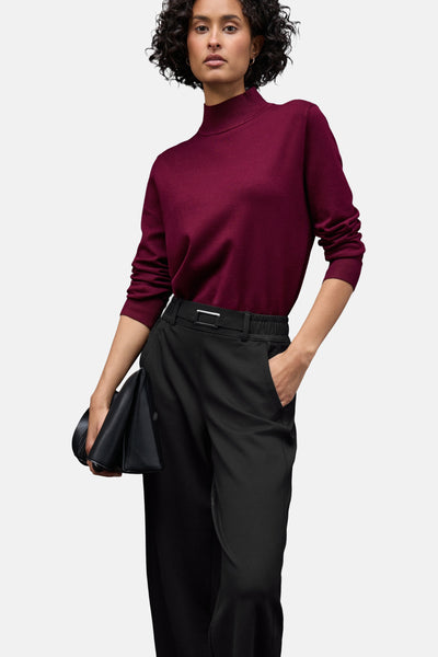 Zwarte kostuumbroek van Street One, gedragen met een bordeauxrode trui en een zwarte clutch.