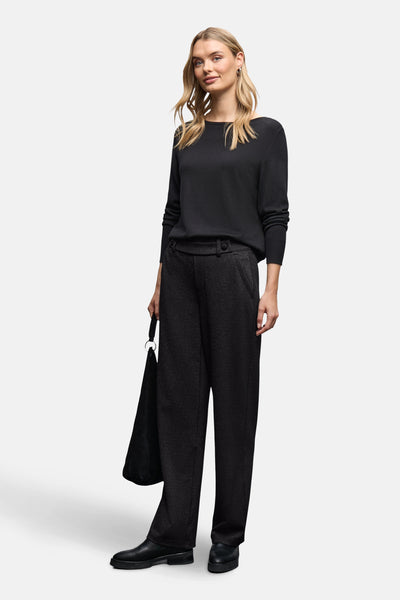 Pantalon noir de Street One, avec une texture subtilement scintillante, porté avec un pull noir et des chaussures plates.
