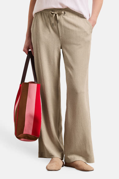 Pantalon beige ample de STREET ONE à la texture gaufrée, avec cordon de serrage, porté avec un sac rayé multicolore et des mules beiges.