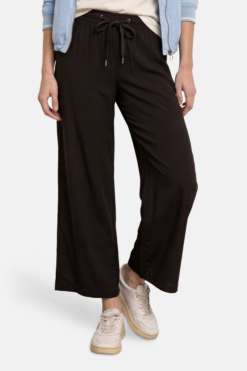 Zwarte broek van STREET ONE met trekkoord in de taille, wijde pasvorm, gedragen met een bomberjack en sneakers.