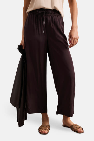 Pantalon brun fluide de STREET ONE avec taille élastiquée et cordon, porté avec un haut clair et des sandales tressées.