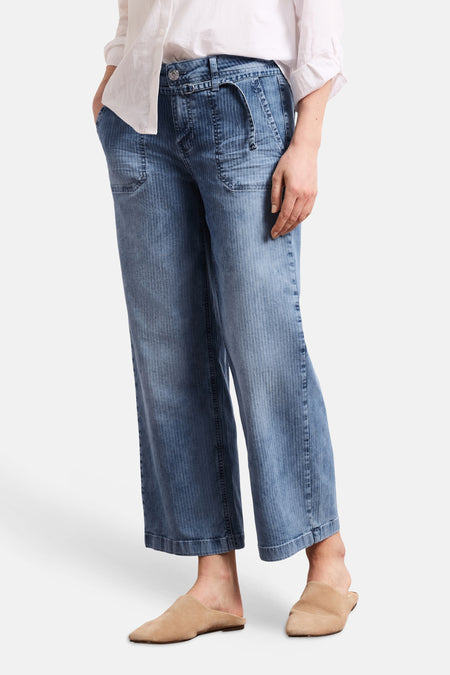 Jean large en denim bleu moyen de STREET ONE à fines rayures verticales, avec sangle décorative, porté avec une chemise blanche et des mules beiges.