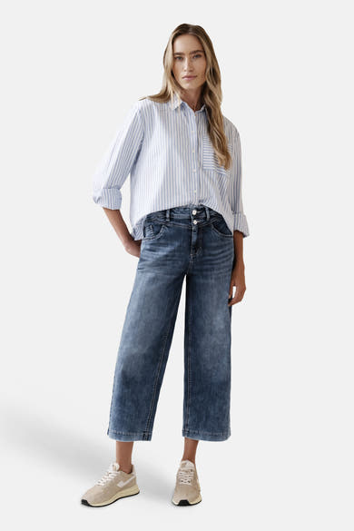 Jean large en denim bleu moyen de STREET ONE, porté avec une chemise rayée bleu et blanc et des baskets beiges.

