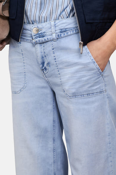 Jean large en denim bleu clair de STREET ONE, avec coutures apparentes, bouton logoté, et main dans la poche, vue rapprochée.