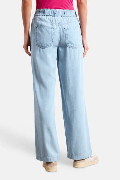 Jean large en denim bleu clair de STREET ONE avec taille élastiquée, poches arrière, porté avec un top rose et des baskets beiges.