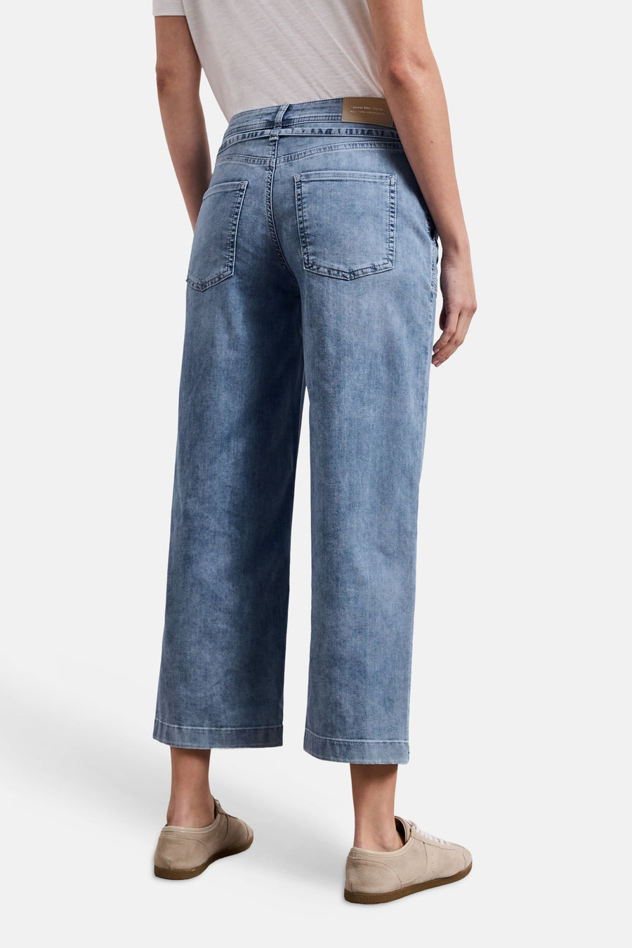 Wijde mid-blue denim jeans van STREET ONE, achterkant, met opgestikte zakken en leren etiket in de taille, gedragen met een wit T-shirt en beige suède sneakers.