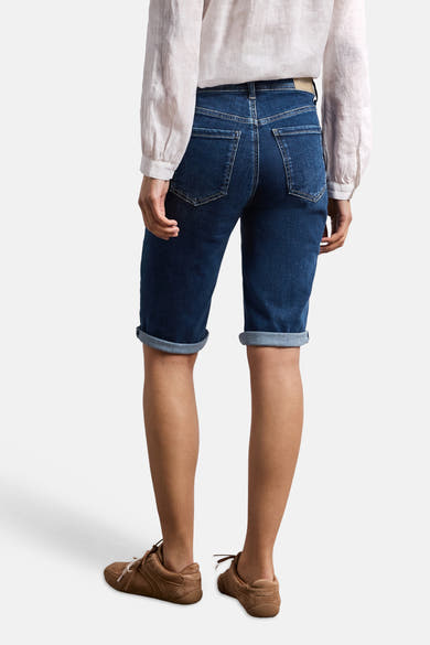 Bermuda en denim bleu moyen de STREET ONE, avec revers et poches arrière, vu de dos, porté avec une chemise claire et des baskets marron.