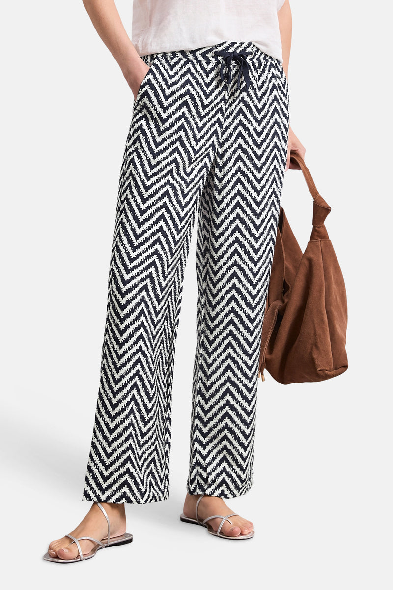 Multicolored wide-leg elastic waist trousers with navy and white zigzag pattern, side view, worn with silver sandals and brown tote bag