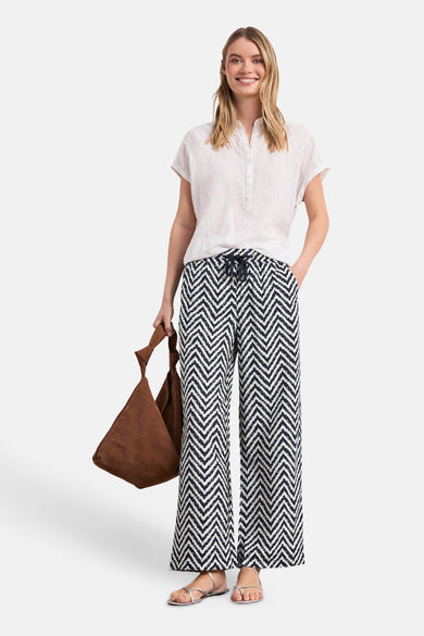 Multicolored wide-leg elastic waist trousers with black and white zigzag pattern, front view, worn with white top and brown bag