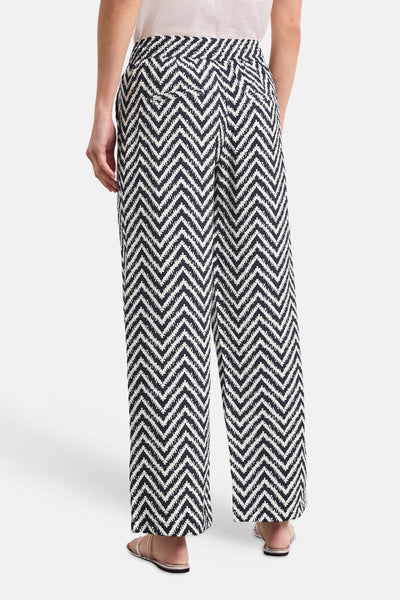 Multicolored wide-leg elastic waist trousers with black and white zigzag pattern, back view, worn with light top and sandals