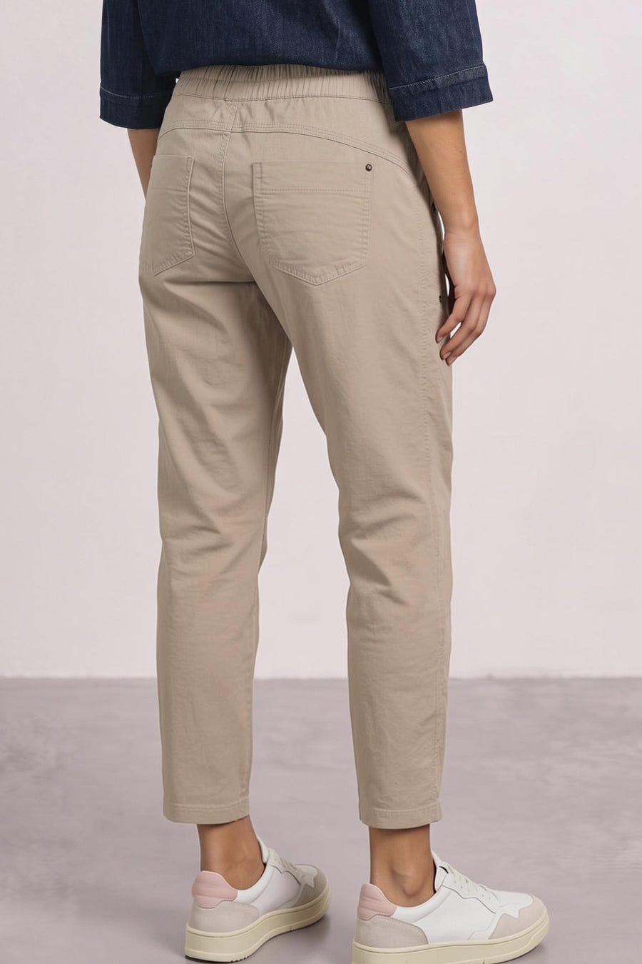 Beige cotton pants with elastic waistband, back pockets, and tapered legs, shown from back view on model wearing navy shirt and white sneakers