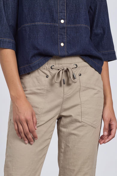 Beige cotton pants with drawstring waist and front pockets, worn with a navy button-up shirt, front view
