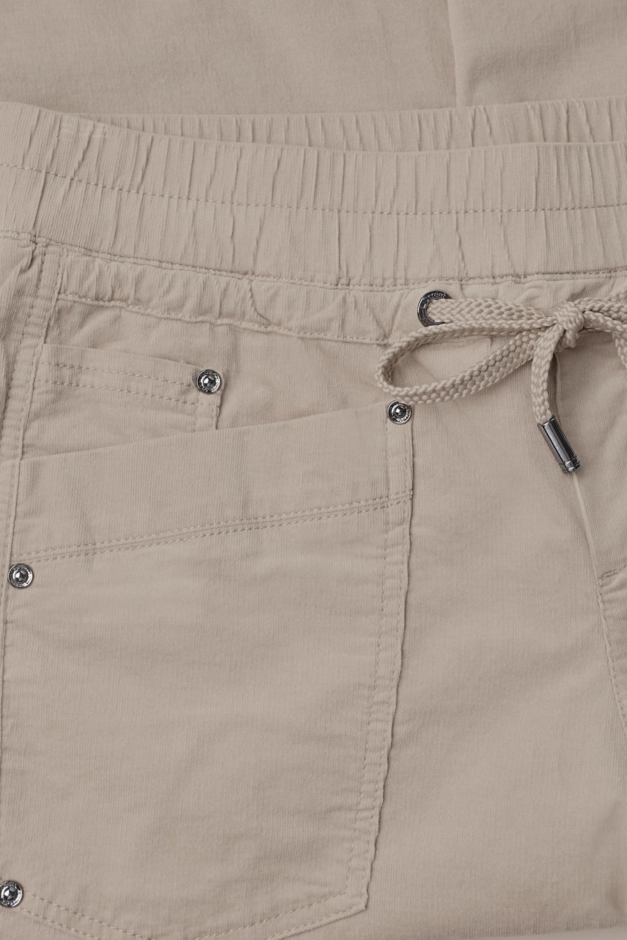 Beige cotton pants with elastic waistband and drawstring, featuring front pockets with silver snap buttons, close-up front view