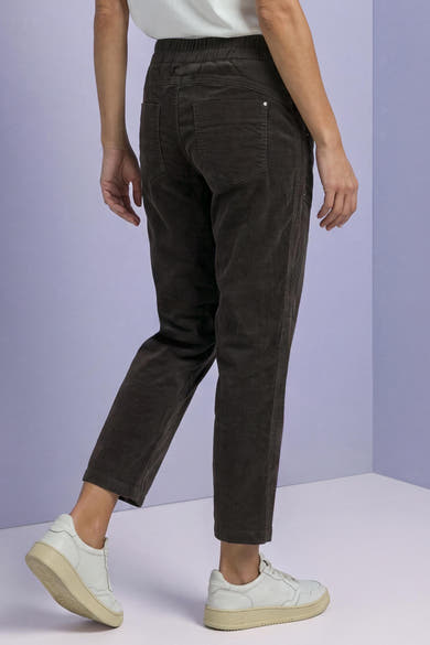 Brown corduroy pants by STREET ONE, back view with elastic waist, two rear pockets, and cropped tapered legs, worn with white sneakers.