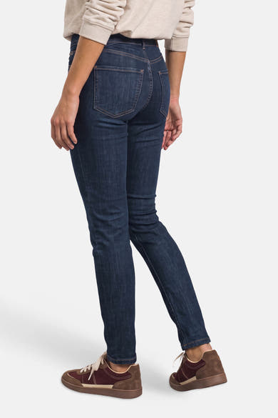Dark blue slim-fit denim jeans by STREET ONE, back view showing clean stitching and classic five-pocket design, worn with beige sweater and brown sneakers.