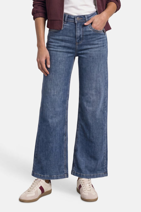 Jean large en denim bleu porté avec une veste bordeaux et des baskets claires, vue de face.