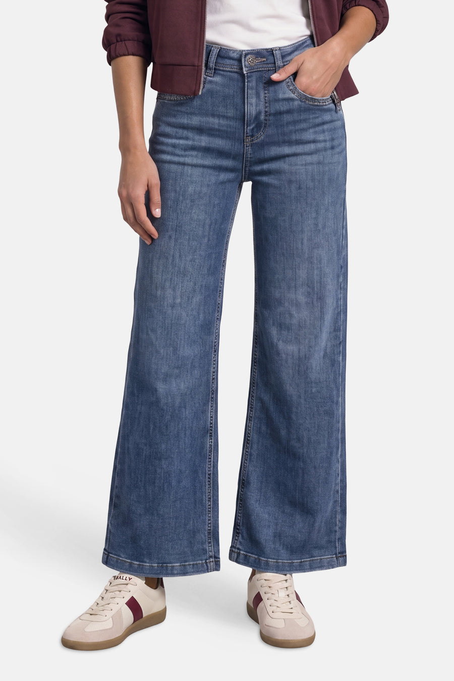 Jean large en denim bleu porté avec une veste bordeaux et des baskets claires, vue de face.