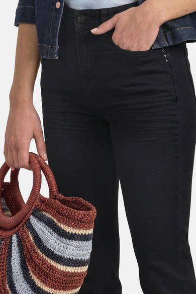 Jean bootcut noir STREET ONE porté, avec une main dans la poche et un sac à rayures colorées.