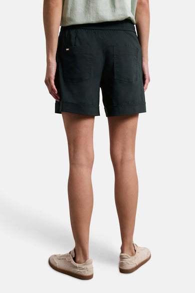 Dark green cotton shorts with rolled cuffs and back pockets, shown from the back on a model wearing a light green top and beige sneakers.