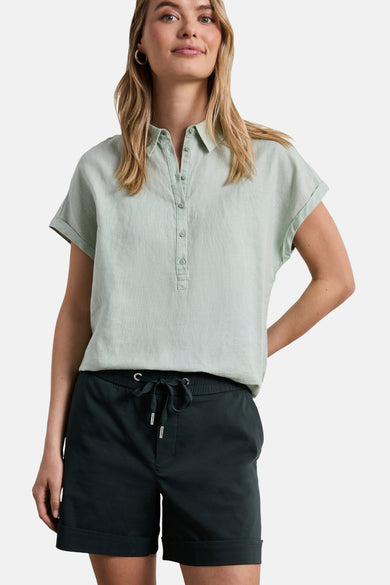 Dark green cotton shorts with drawstring waist and cuffed hem, front view on model wearing light green button-up top.