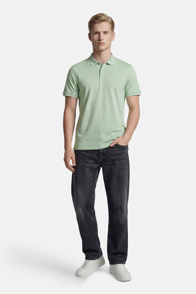 Groen poloshirt met korte mouwen, knoopkraag en discreet logo van Levi's®, gedragen met een zwarte, uitgewassen spijkerbroek en witte sneakers.