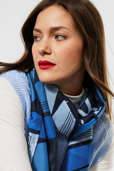 Blue patterned foulard with geometric design, worn by model in side view, paired with light blue knit vest and white top