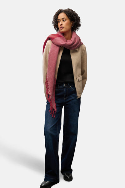 Écharpe rouge par Street One, à motif tissé texturé et franges, portée avec un manteau beige et un jean bleu.

