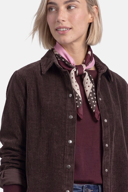 Multicolored foulard with polka dot pattern and pink border, worn as neck scarf with corduroy jacket and maroon sweater, side view close-up
