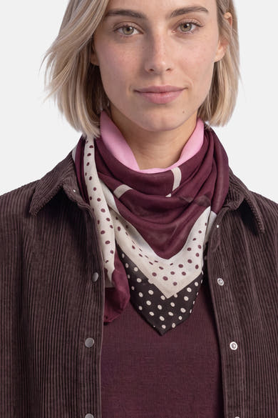 Multicolored foulard with burgundy, cream, and black polka dot patterns worn around neck over pink shirt and corduroy jacket, front view