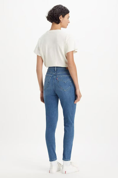 Jean skinny bleu denim par Levi's®, avec une coupe rétro, porté avec un t-shirt blanc et des chaussures de sport blanches.