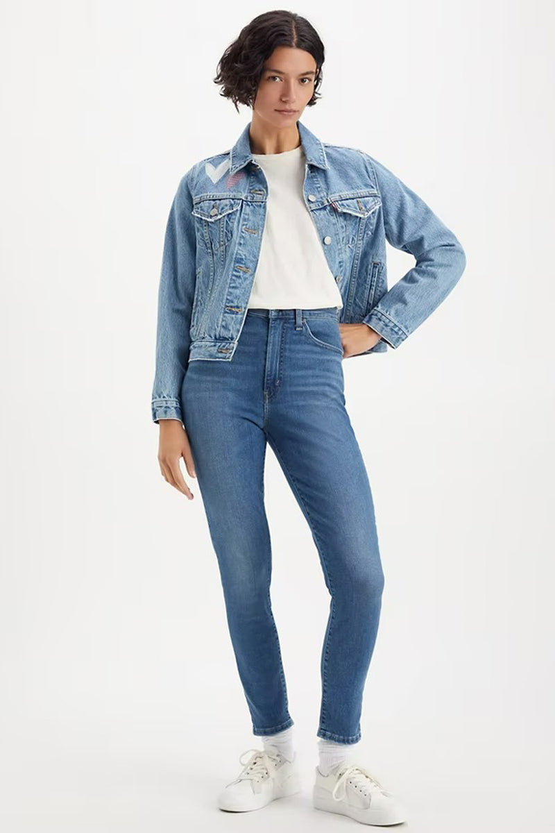 Jean skinny bleu moyen de Levi's, porté avec une veste en jean et des baskets blanches.