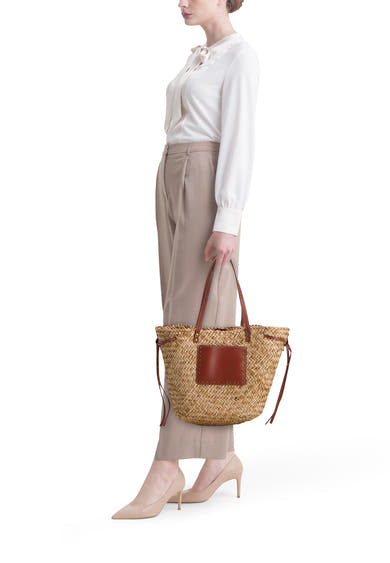 Sac à bandoulière beige de STREET ONE en paille tressée avec empiècement en cuir marron, porté par une femme élégante.