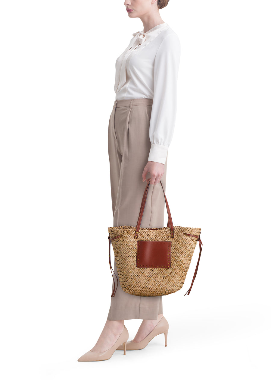 Sac à bandoulière beige de STREET ONE en paille tressée avec empiècement en cuir marron, porté par une femme élégante.