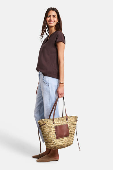Sac à bandoulière en paille beige de STREET ONE avec poignées et empiècement en cuir marron clouté, porté de côté.
