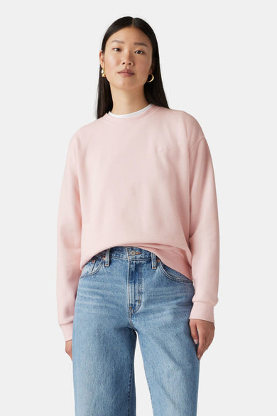Sweat rose de Levi's® porté avec un jean bleu et des boucles d'oreilles dorées.