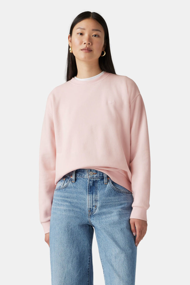 Sweat rose de Levi's® porté avec un jean bleu et des boucles d'oreilles dorées.