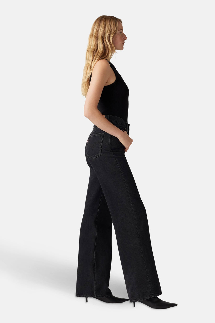 Jean large en denim noir de Levi's, porté avec un débardeur noir et des bottines en cuir, vue de côté.
