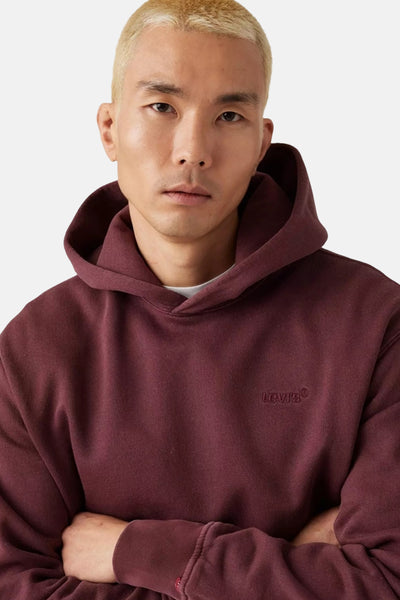 Sweat à capuche bordeaux de Levi's, porté par un mannequin aux cheveux blonds platine.