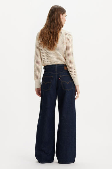 Jean droit en denim bleu foncé de Levi's, avec poches arrière et porté avec un pull en maille ajourée.