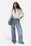 Levi's® middendonkerblauwe spijkerbroek met rechte pijpen, met een strikceintuur en een persoon die een witte blouse draagt.